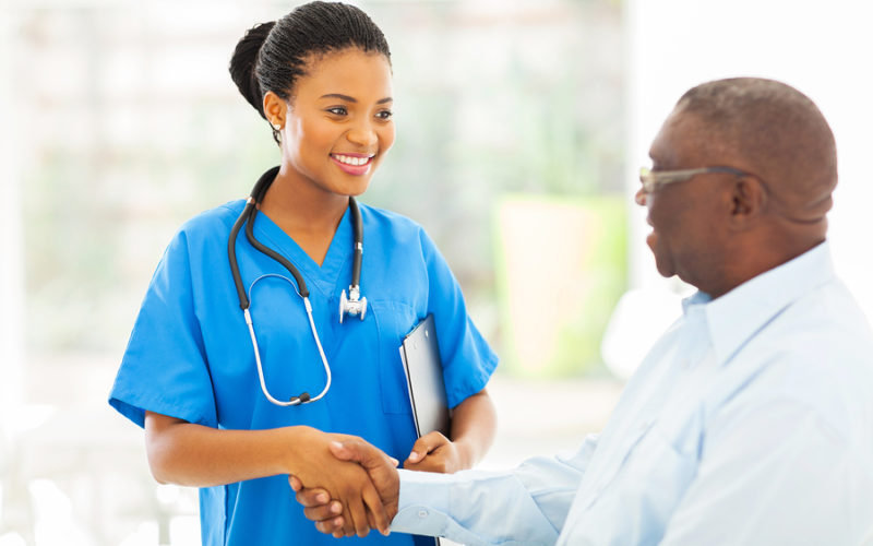 amable enfermera afroamericana estrechando la mano de un paciente mayor